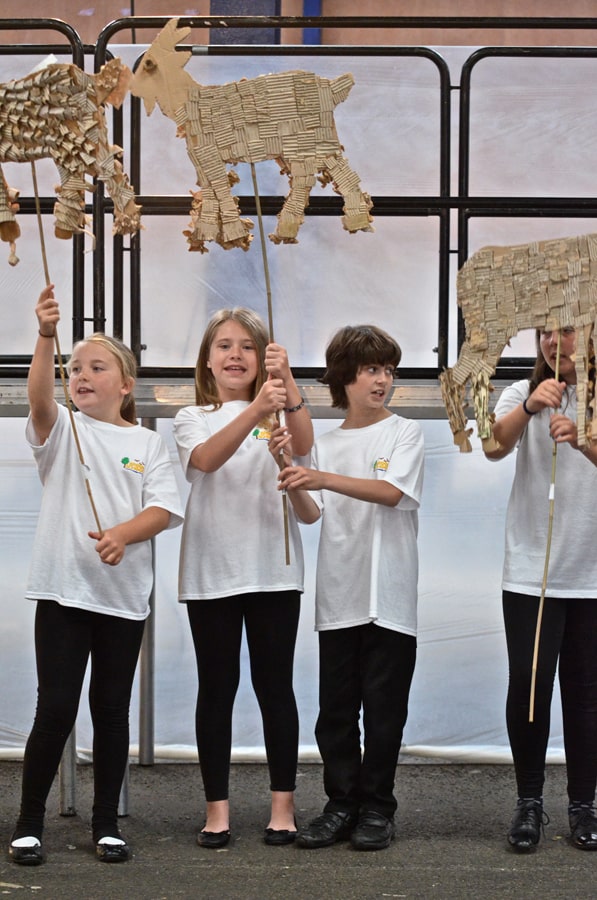 Four smiling children in white t shirts with school logo holding crafted animal banners