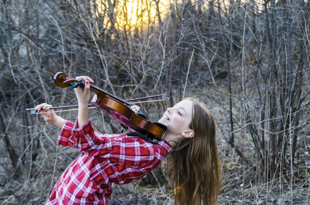 Happy child plays the violin in an outside setting