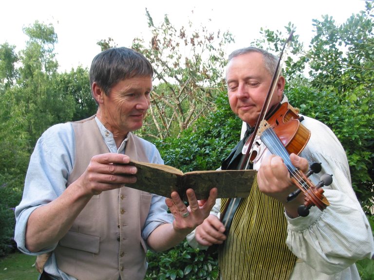 Two folk musicians, one with fiddle, look at open book