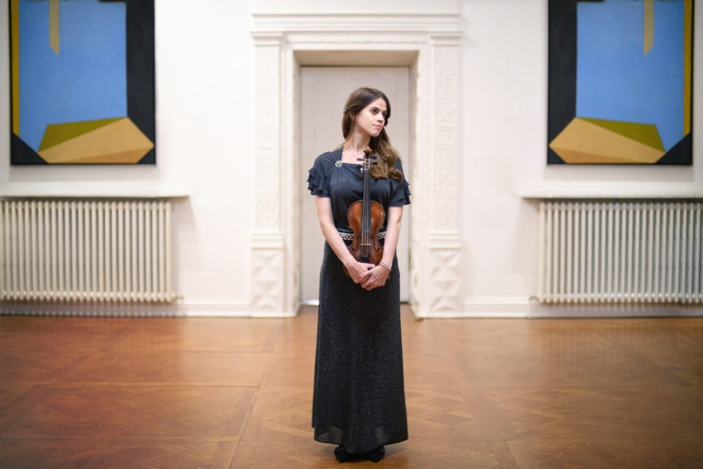 Woman holding violin stands alone in hall
