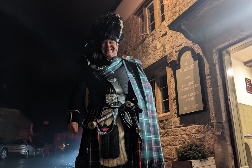 Happy bagpiper stands outside pub on a dark night