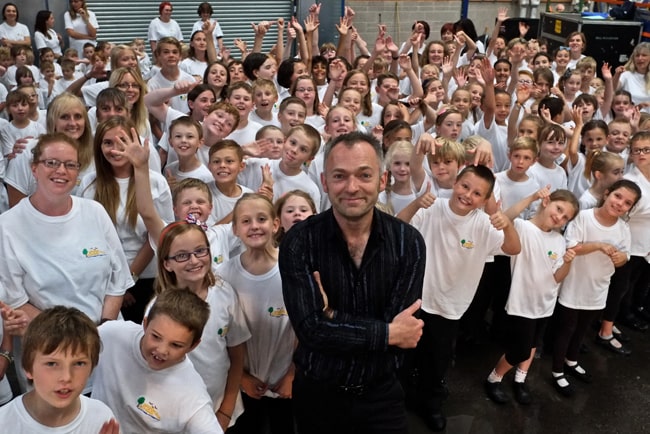 Teacher stands surrounded by happy school children